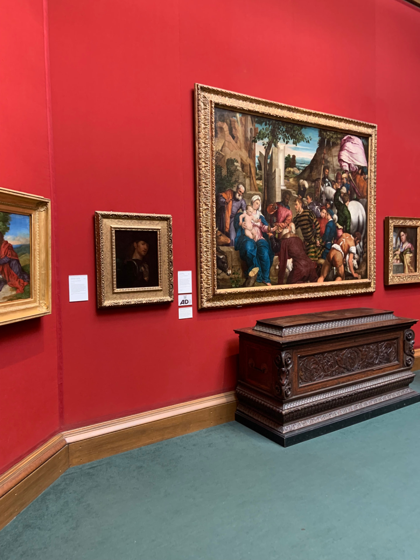 Old master paintings displayed against a red gallery wall